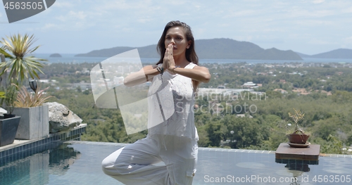 Image of Calm tourist standing in balance pose poolside against town on tropical coast