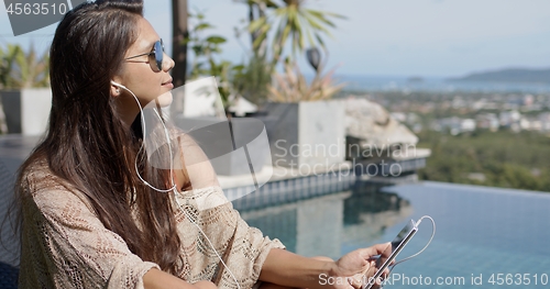 Image of Woman listening to music at poolside and enjoying sunny day