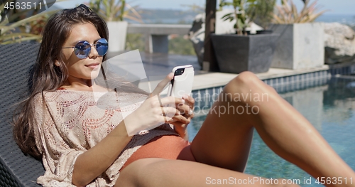 Image of Stylish woman using smartphone at poolside