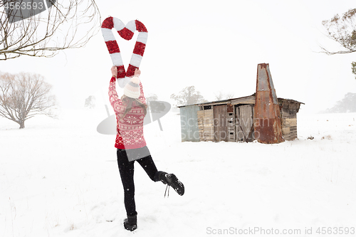 Image of Woman holding Christmas candy canes in shape of heart in snow landscape