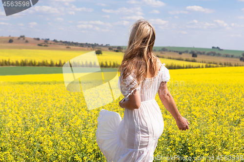 Image of Woman in white dress looking out over fields of golden canola