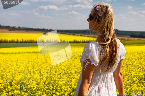 Image of Woman in white dress standing by fields of golden canola