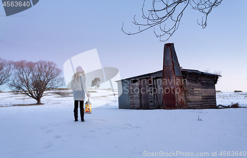 Image of A woman standing in a snow field holding lantern at dusk