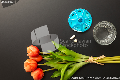 Image of open pillbox with some pills glass of water and tulips