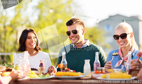 Image of happy friends eating and drinking at rooftop party