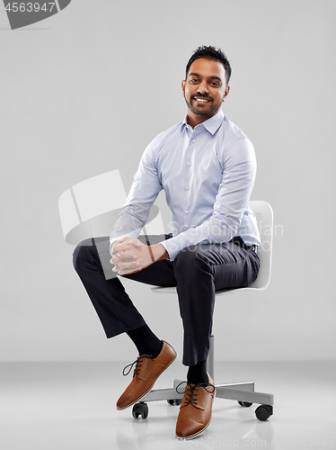 Image of smiling indian businessman sitting on office chair