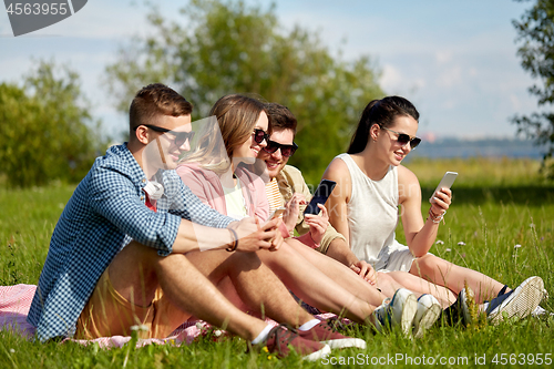 Image of smiling friends with smartphones sitting on grass