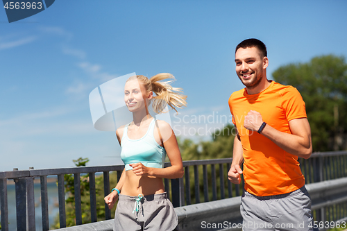 Image of couple with fitness trackers running along bridge