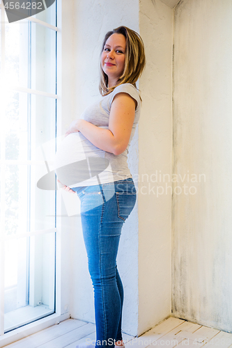 Image of Beautiful pregnant woman standing near window