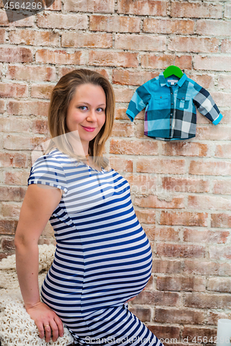 Image of Beautiful pregnant woman sitting near wall