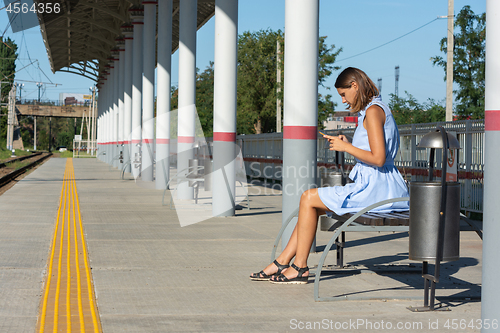 Image of Young girl looks at the phone on the empty platform of the railway station