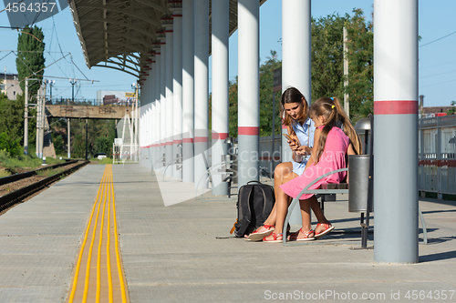 Image of Mom and daughters are waiting for the train on the empty platform of the railway station