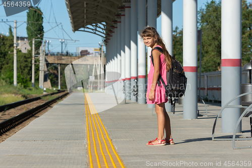 Image of The eight-year-old girl on the platform of the railway station turned around and looked into the frame