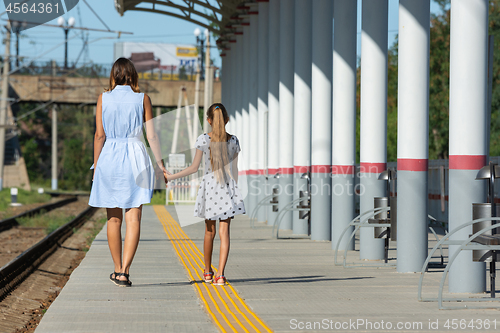 Image of Young beautiful girl and teenage daughter walk from the camera on the empty platform of the train station