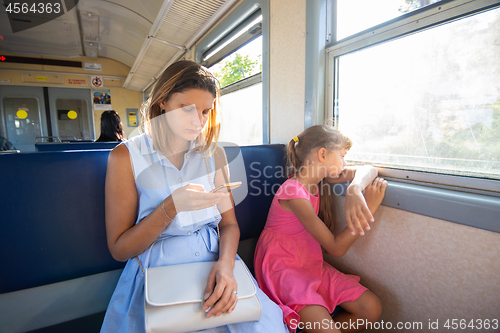 Image of A young girl looks at the phone, daughter at the window in the electric train
