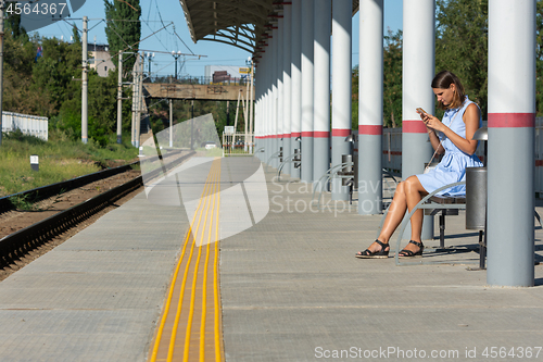 Image of Young girl with a phone waits for a train on the empty platform of the railway station