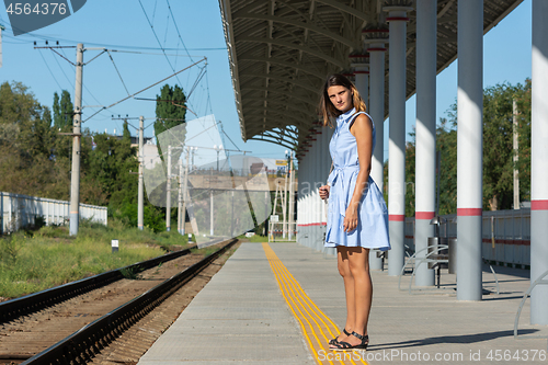 Image of Young beautiful girl stands alone on a railway platform and looks into the distance with anticipation