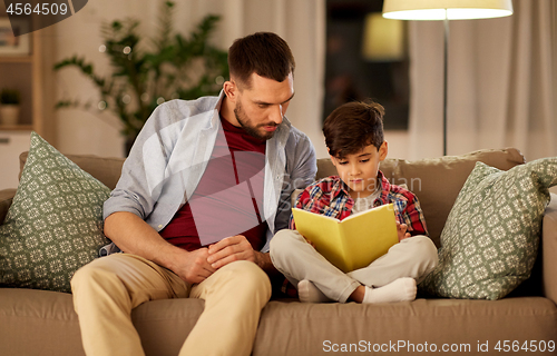 Image of father and son reading book sofa at home