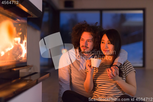 Image of happy multiethnic couple sitting in front of fireplace