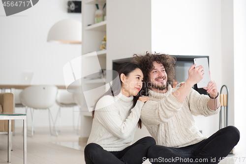 Image of multiethnic couple using tablet computer in front of fireplace