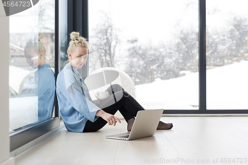 Image of woman drinking coffee and using laptop at home