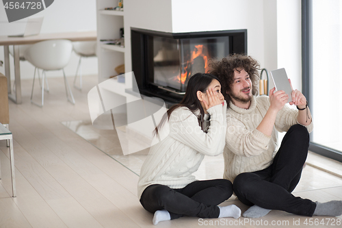 Image of multiethnic couple using tablet computer in front of fireplace