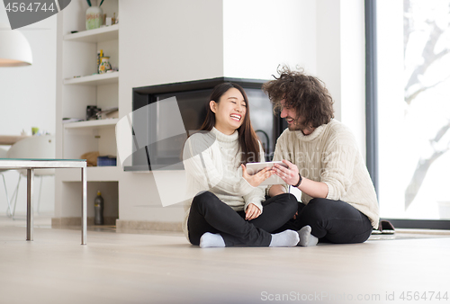 Image of multiethnic couple using tablet computer in front of fireplace