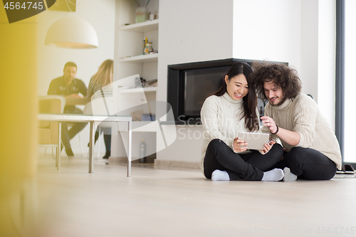 Image of multiethnic couple using tablet computer in front of fireplace