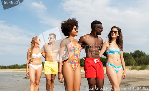 Image of happy friends walking along summer beach