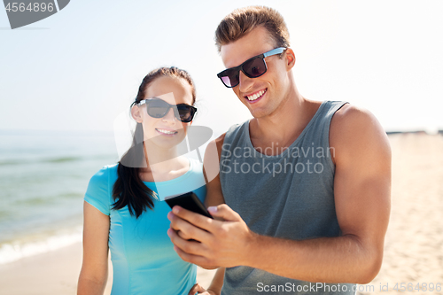 Image of couple in sports clothes with smartphones on beach