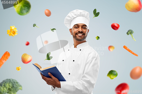 Image of happy indian chef with cookbook over vegetables