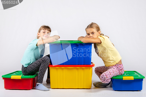 Image of Two girls are sitting on large boxes for toys and looked into the frame