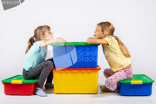 Image of Two girls sit on big boxes for toys and show each other tongue