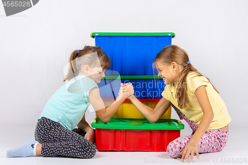 Image of Two girls fight on hands, putting elbows on a box with toys