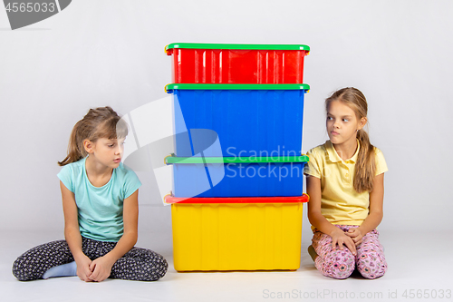 Image of Two girls look at each other hiding behind large plastic boxes in the middle between them