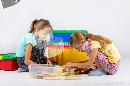 Image of Two girls sit on the floor and collect a toy house