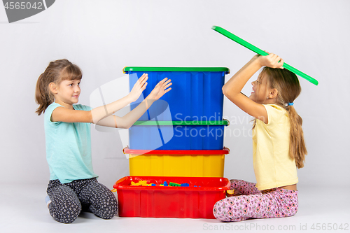 Image of A girl pretending to be a hundred wants to throw a toy box lid on another girl