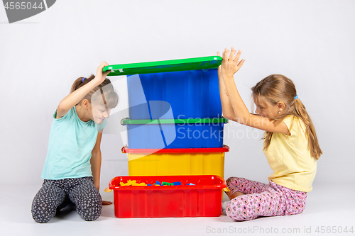 Image of Two girls opened the lid of a large plastic box with toys, and look inside