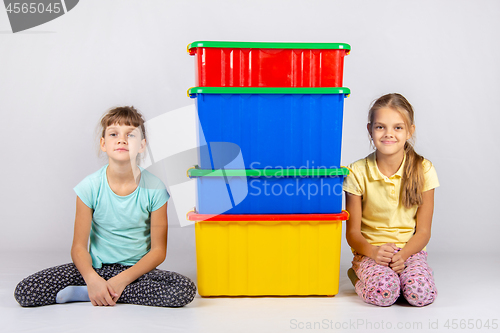 Image of Two girls are sitting next to four large plastic boxes