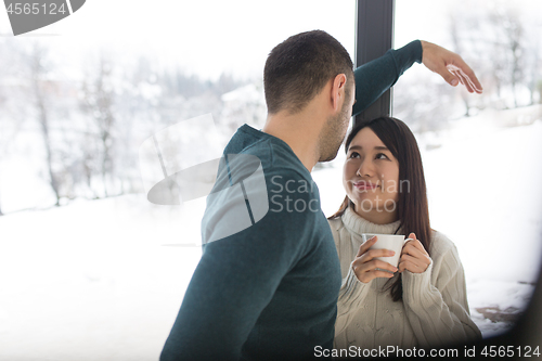 Image of multiethnic couple enjoying morning coffee by the window