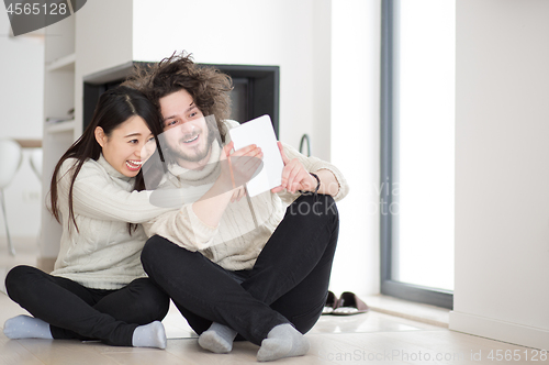 Image of multiethnic couple using tablet computer in front of fireplace