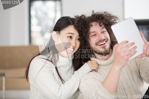 Image of multiethnic couple using tablet computer in front of fireplace