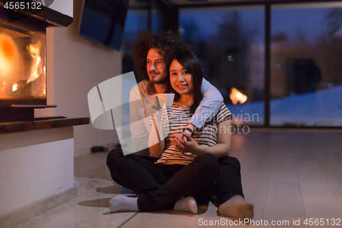 Image of happy multiethnic couple sitting in front of fireplace