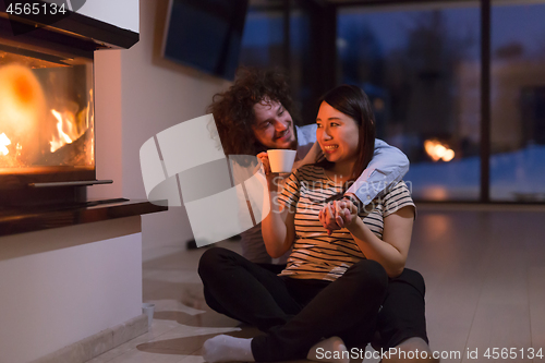 Image of happy multiethnic couple sitting in front of fireplace