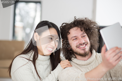 Image of multiethnic couple using tablet computer in front of fireplace