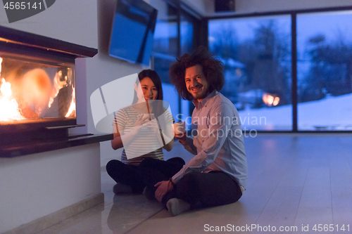 Image of happy multiethnic couple sitting in front of fireplace