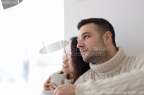 Image of multiethnic couple enjoying morning coffee by the window