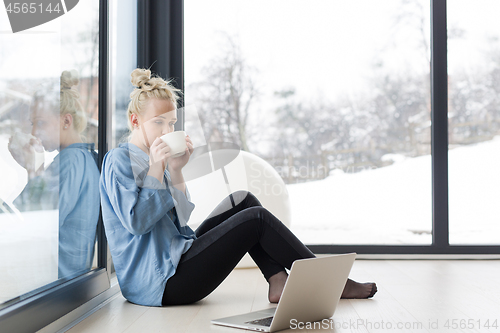 Image of woman drinking coffee and using laptop at home