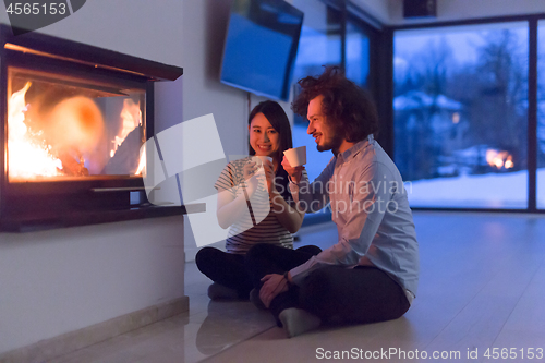 Image of happy multiethnic couple sitting in front of fireplace