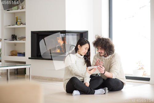 Image of multiethnic couple using tablet computer in front of fireplace